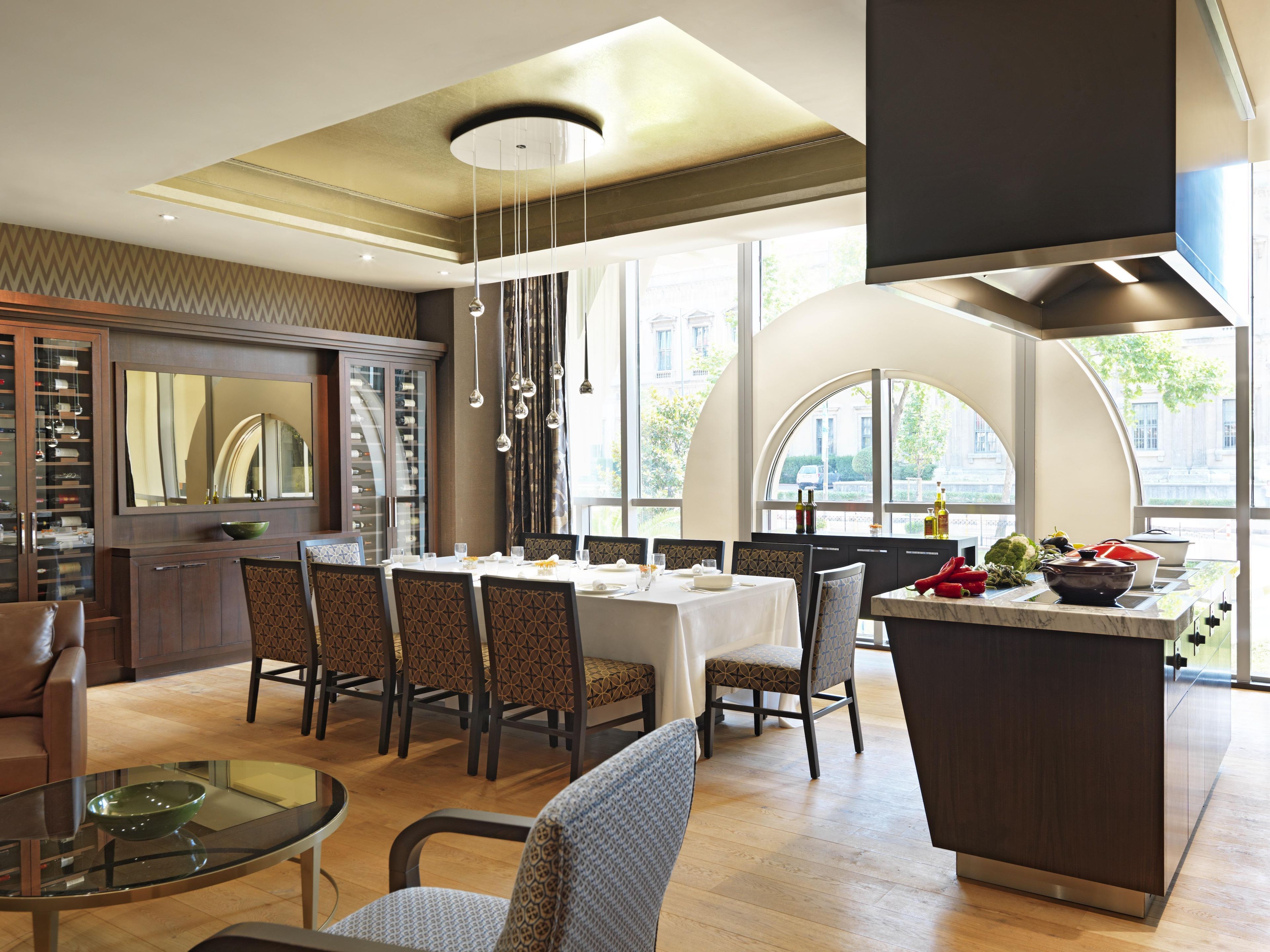 A modern dining area with a central table, chairs, and a kitchen island with a bowl of fruit.