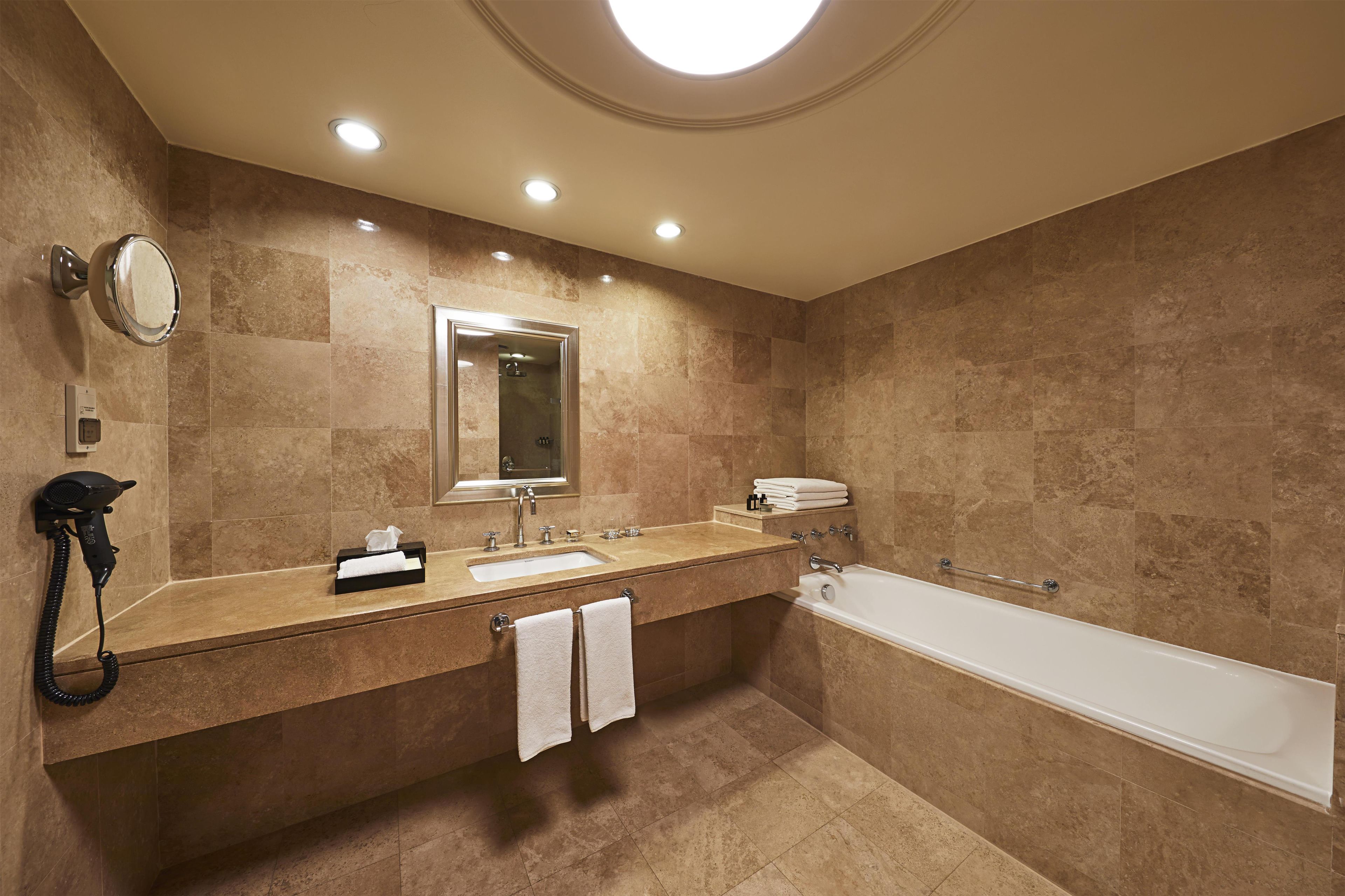 A modern bathroom with a double sink vanity, a large mirror, a built-in bathtub, and recessed ceiling lighting.