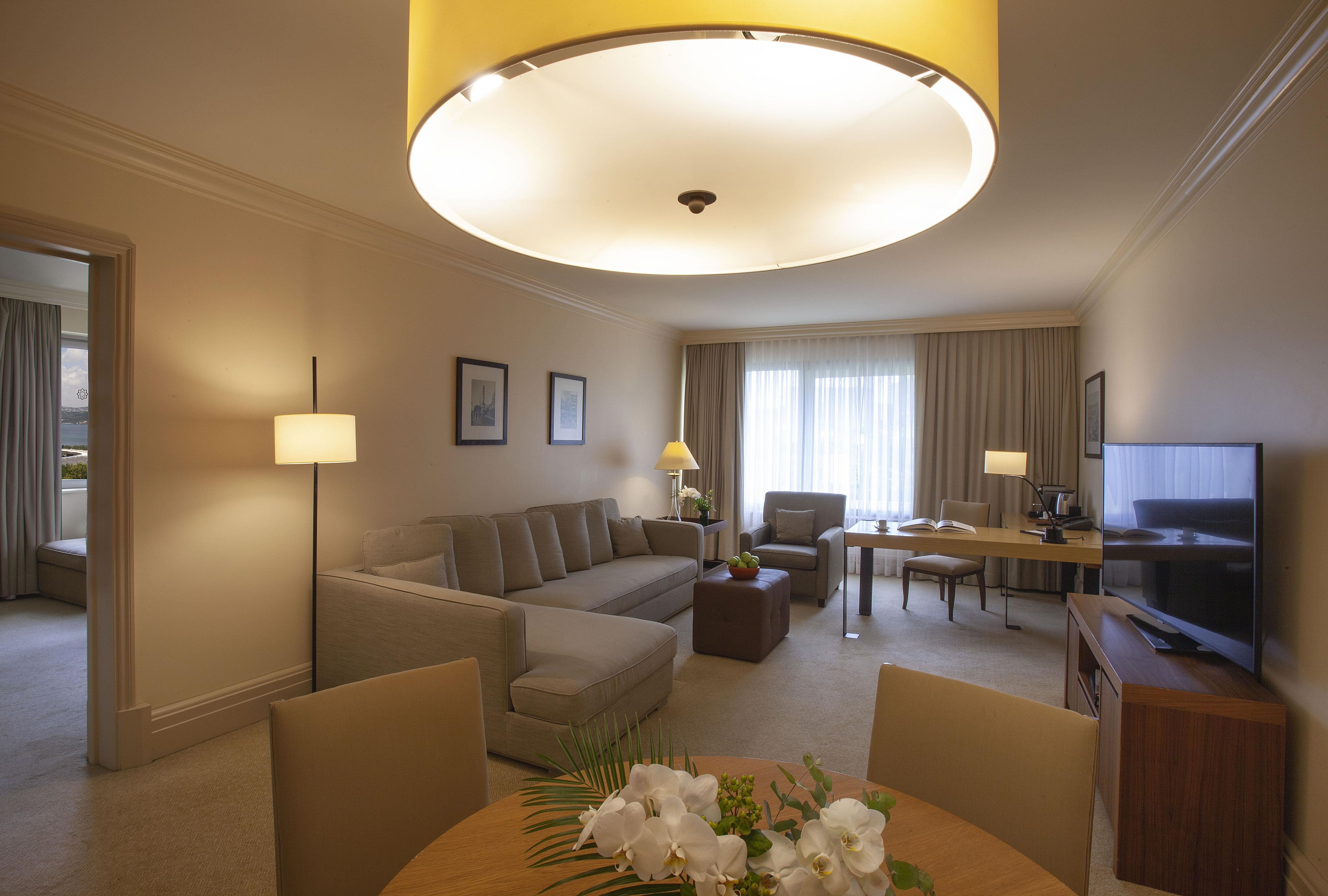 Ein Hotelzimmer mit einer Couch, Sesseln, einem Esstisch, einem Fernseher und einer Lampe.