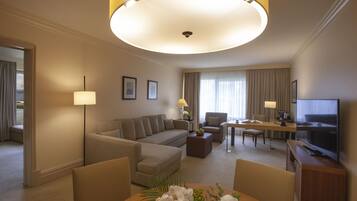 Ein Hotelzimmer mit einer Couch, Sesseln, einem Esstisch, einem Fernseher und einer Lampe.