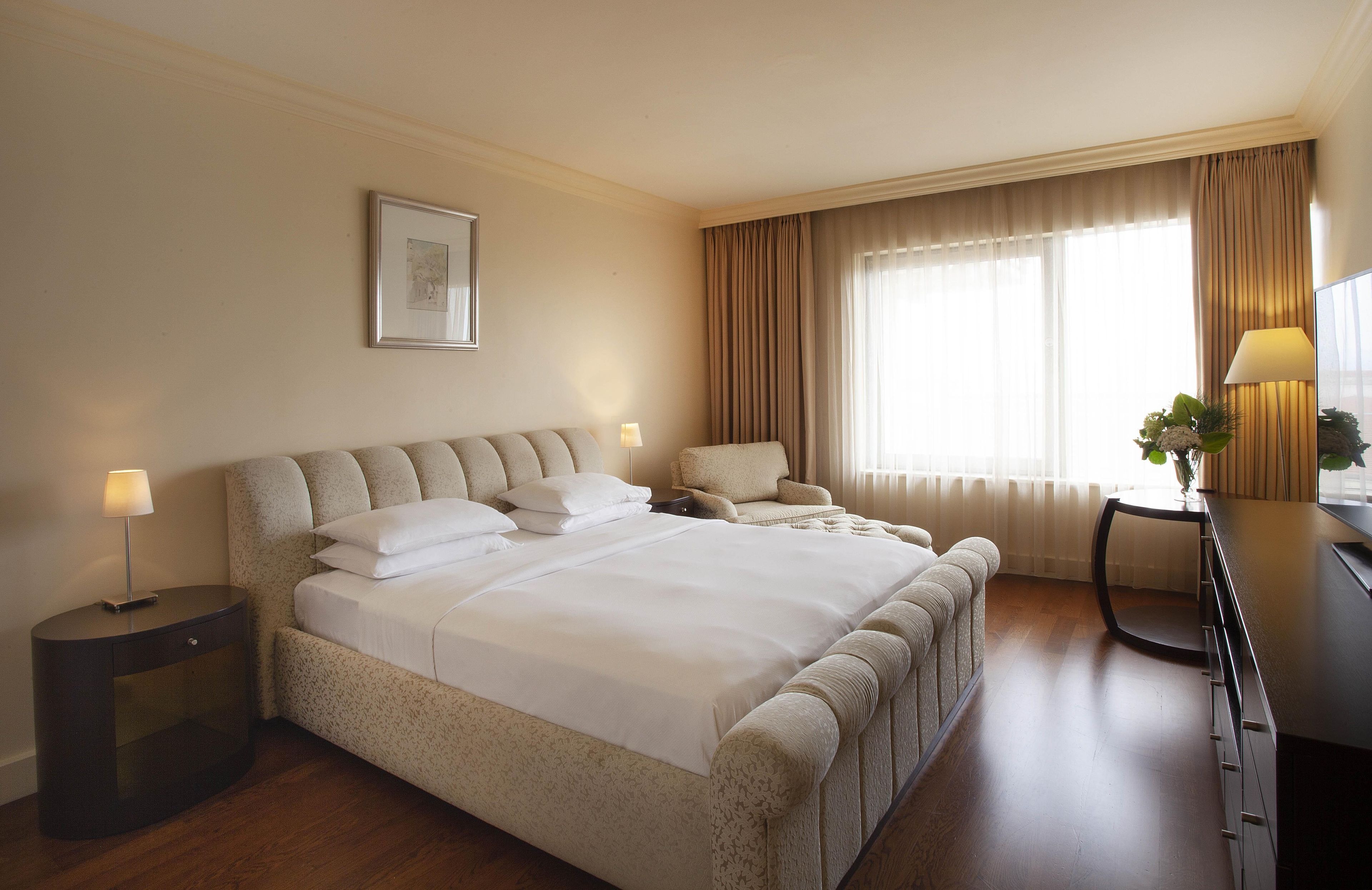 A hotel room with a large bed, a desk, a chair, a lamp, and a window with curtains.