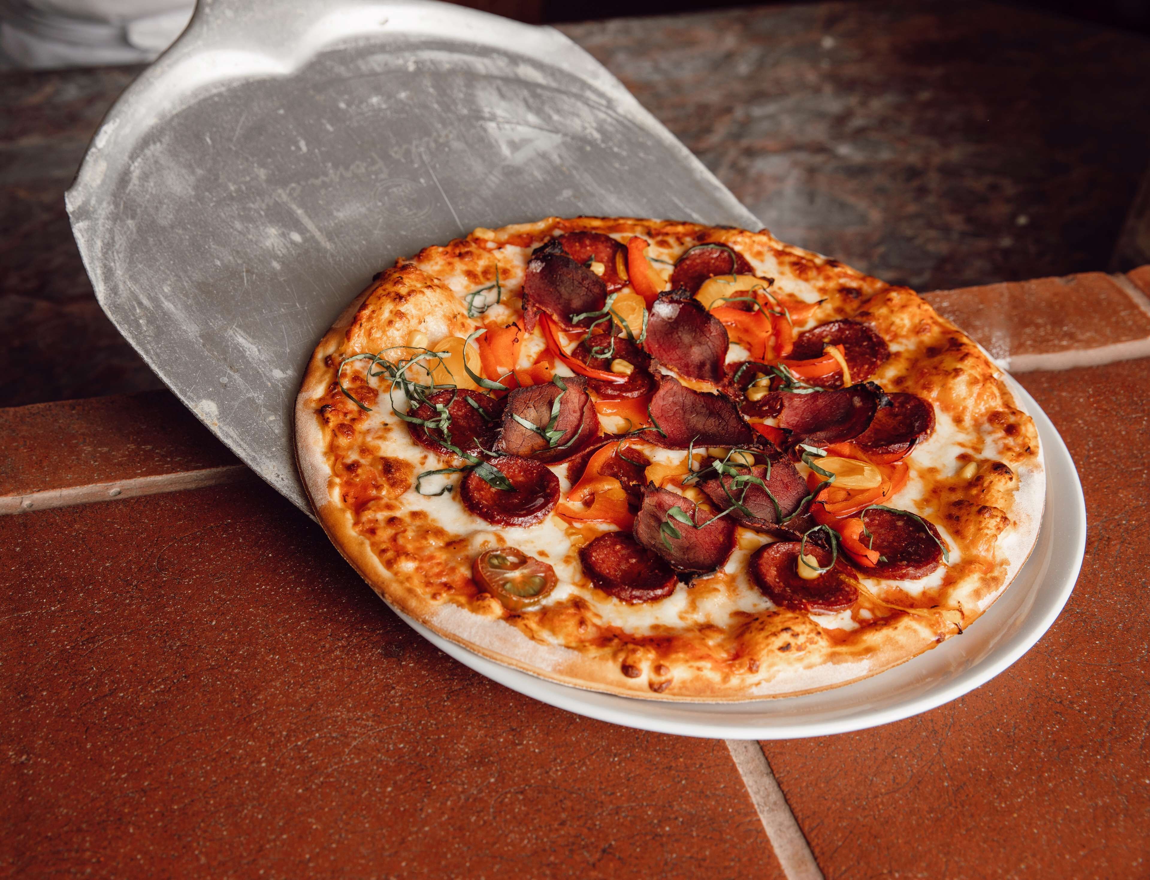 A pizza with pepperoni and vegetables on a white plate.