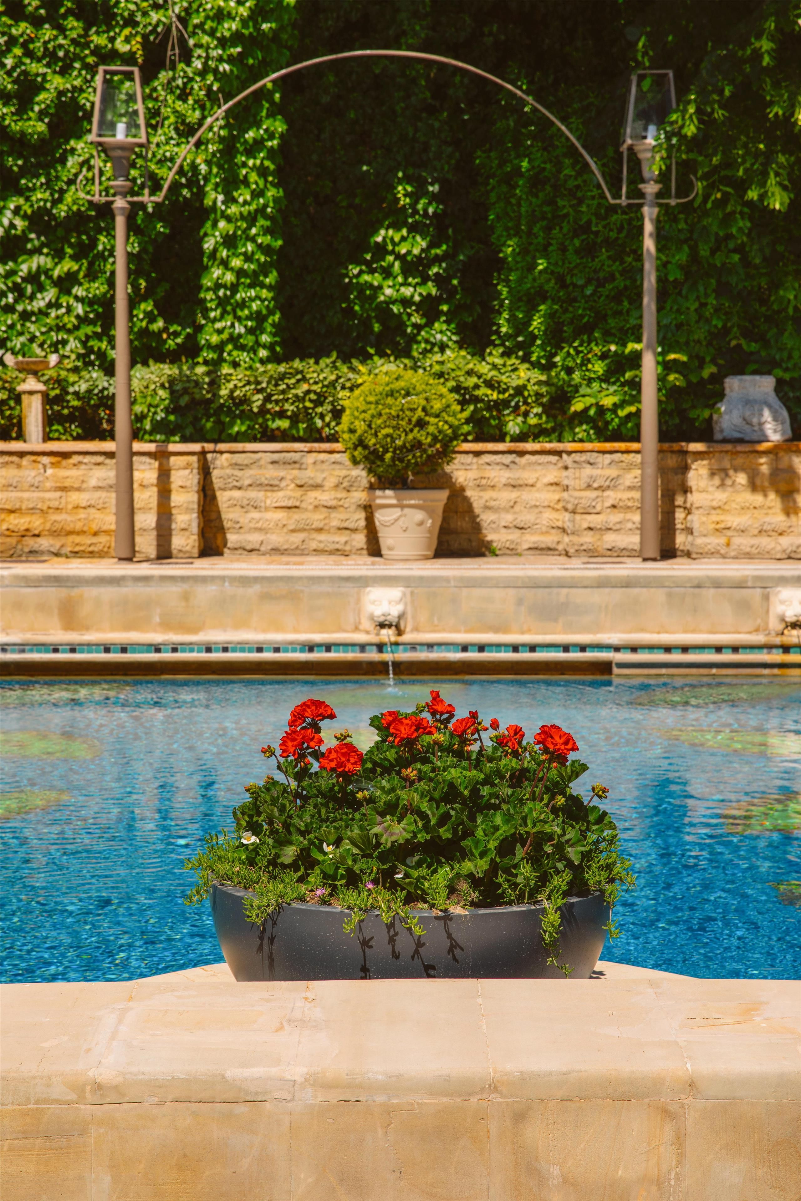 Una piscina con un jardín de flores rojas, un muro de piedra y un farol.