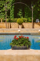 Una piscina con un jardín de flores rojas, un muro de piedra y un farol.