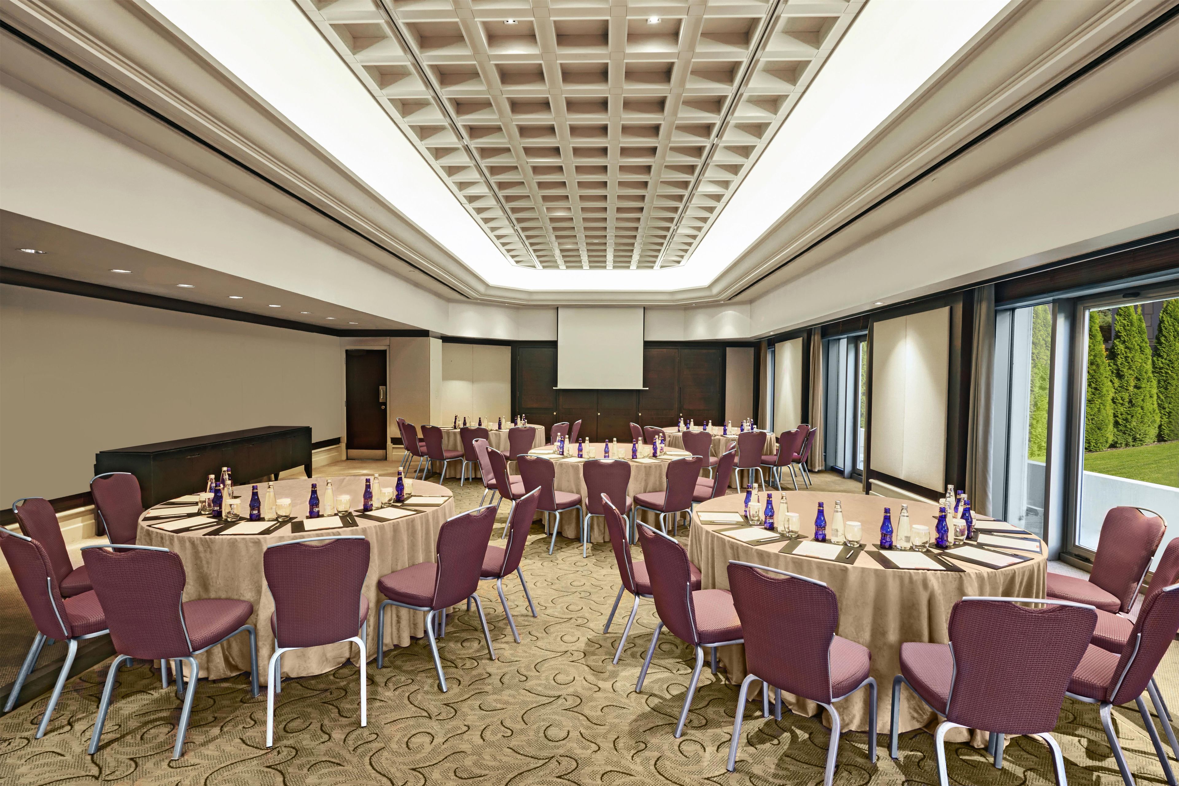 A conference room with round tables, chairs, and a large screen.