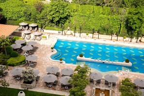 A swimming pool with lounge chairs and umbrellas, surrounded by greenery and a tiled patio area. - Grand Hyatt Istanbul (Istanbul)