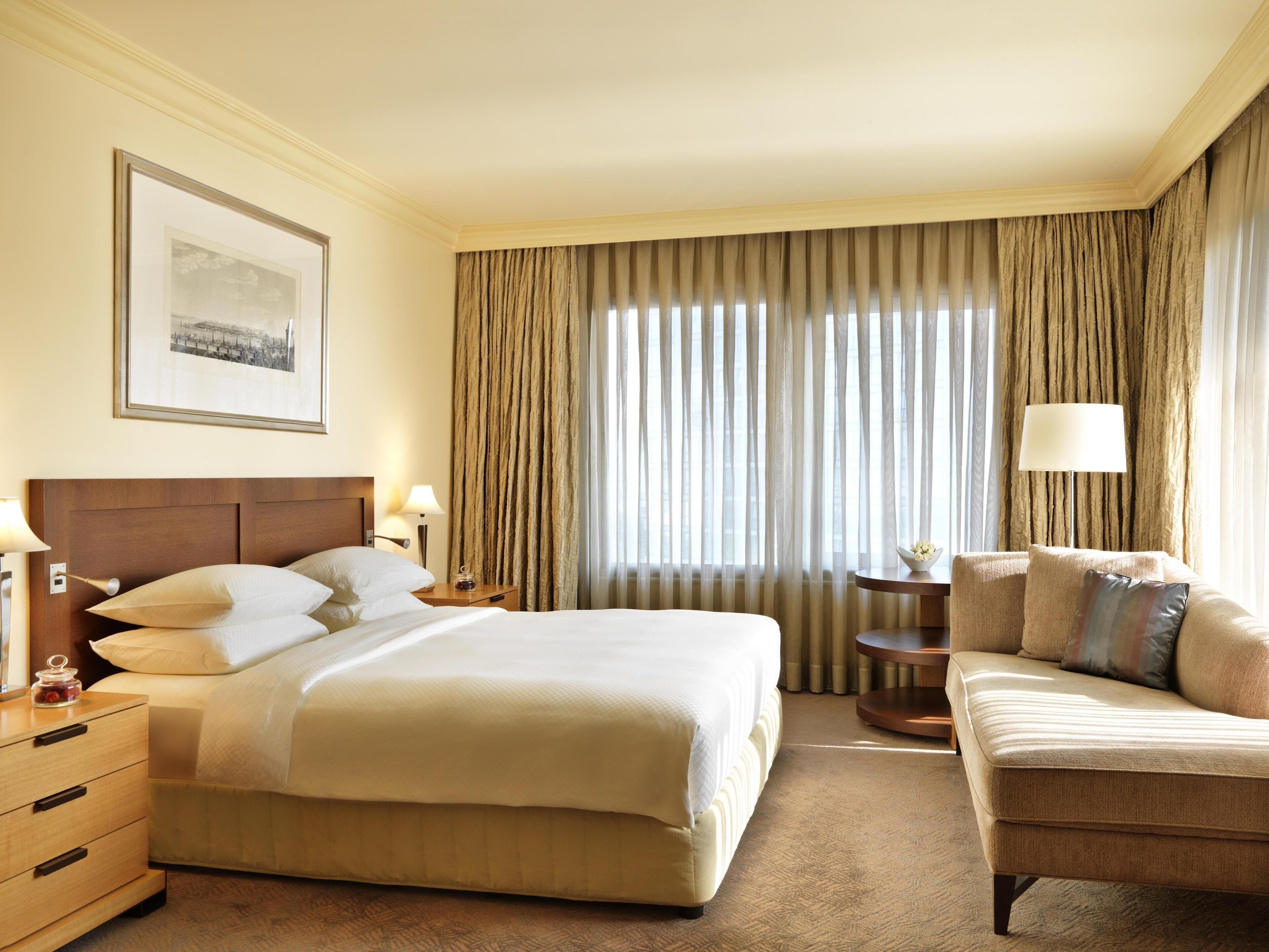A hotel room with a large bed, a sofa, a small table, and a lamp.