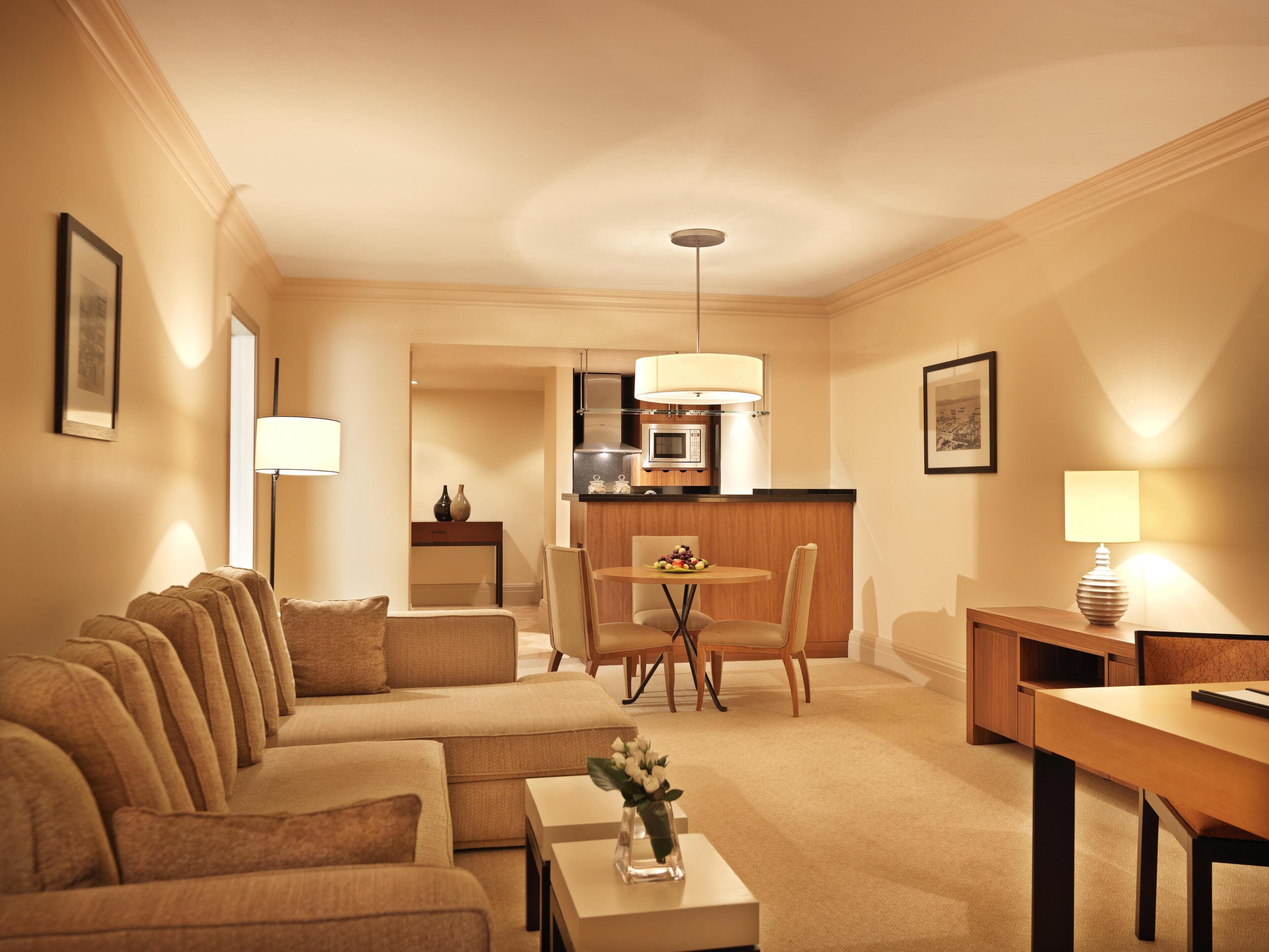 Een hotelkamer met een zithoek, een eettafel, een keukenhoek en een lamp.