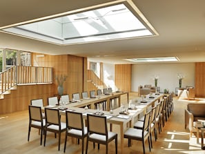 A spacious, modern conference room with a long table and chairs, large windows, and a wooden interior.