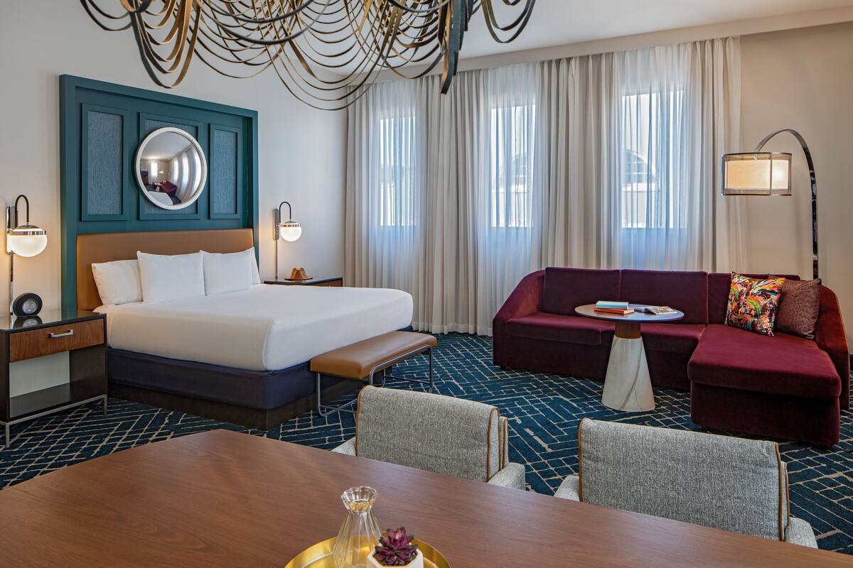 Una habitación de hotel con una cama grande, un sofá rojo, una mesa de comedor y un candelabro.