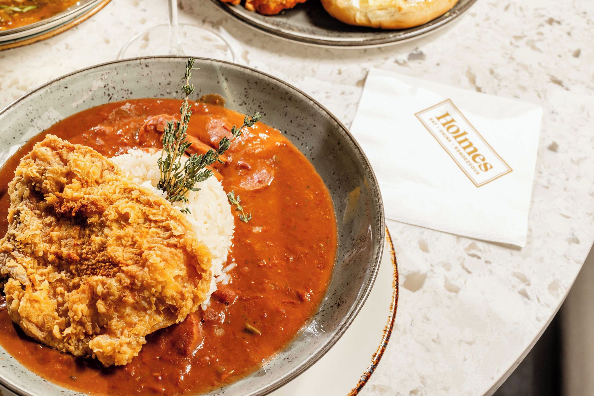 A plate of food with a breaded chicken breast and rice, garnished with a sprig of thyme.