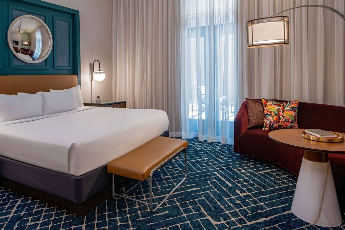 Habitación de hotel con una cama grande, un banco, un sofá, una mesita y un espejo en la pared.
