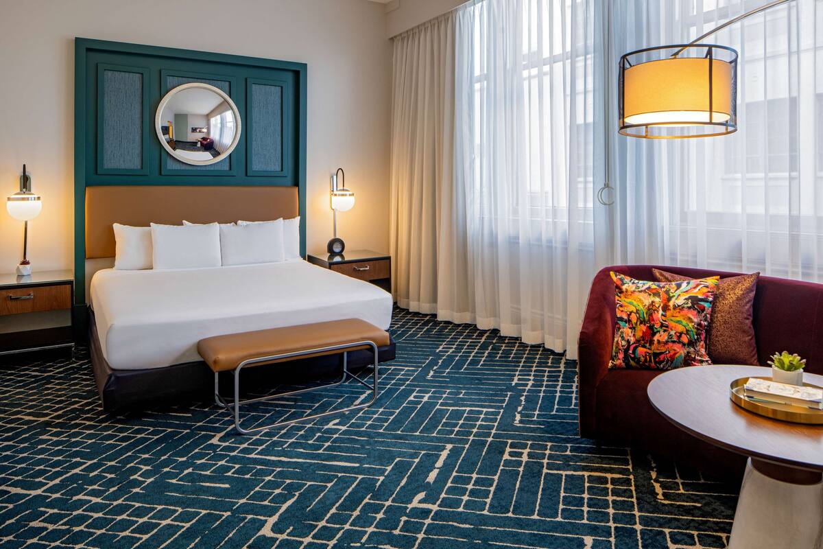 Habitación de hotel con una cama grande, un banco, un sofá, una mesa redonda y un espejo en la pared.