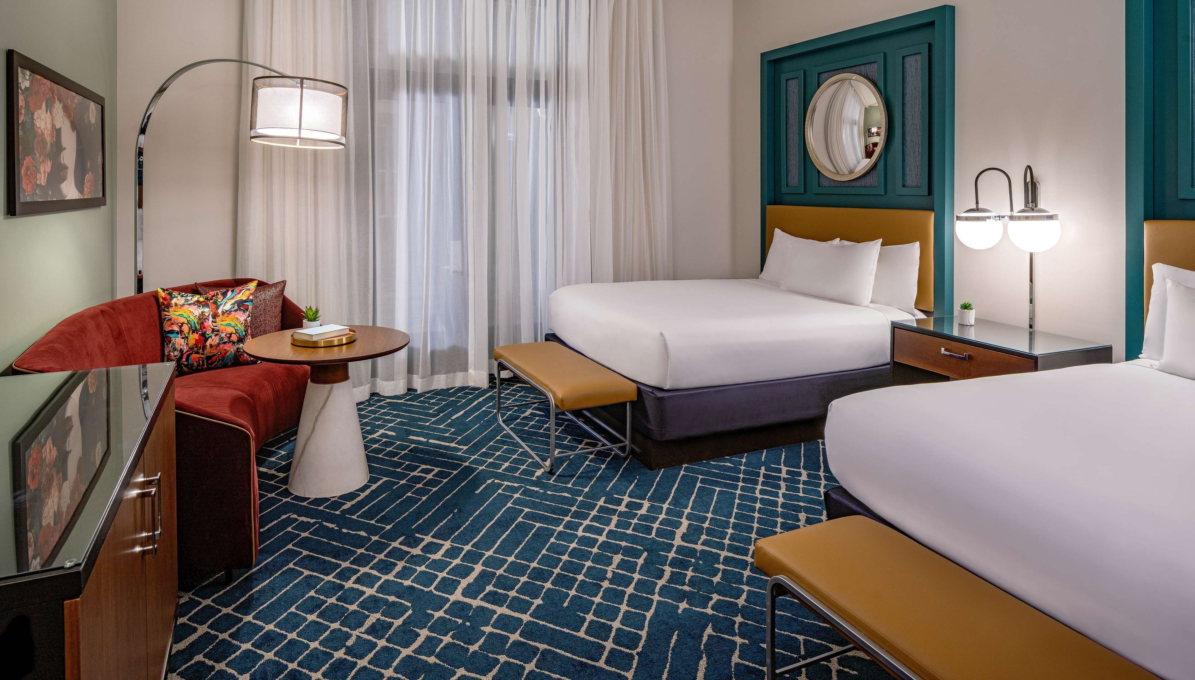Una habitación de hotel con una cama grande, una mesita de noche, un banco, un escritorio y una silla.