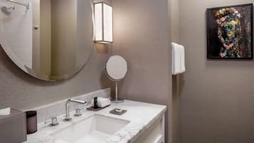 A bathroom with a white marble sink, a round mirror, a towel rack, and a framed artwork on the wall.