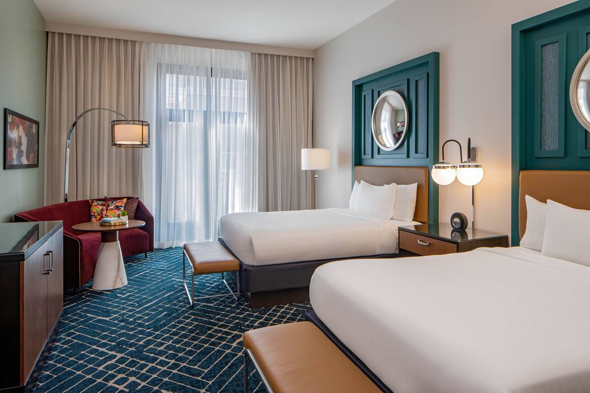 Una habitación de hotel con dos camas, un sofá, un escritorio y un ventanal con cortinas.