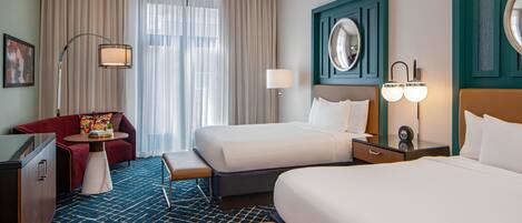 A hotel room with two beds, a sofa, a desk, and a large window with curtains.