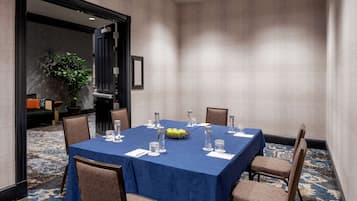 Un salón de conferencias con mantel azul, sillas dispuestas y una cesta de fruta.