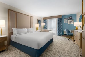 A hotel room with a large bed, a desk, two chairs, a small table, and a window with curtains. - DoubleTree by Hilton Wilmington, NC (Wilmington)