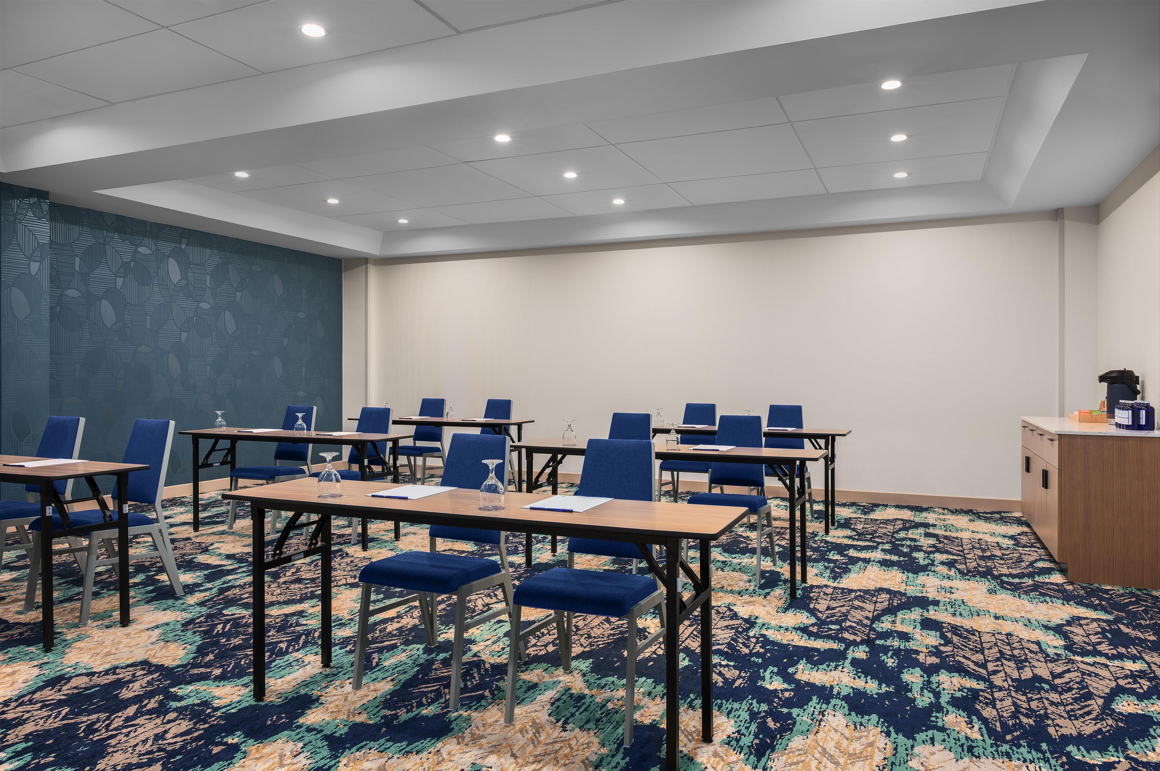 A conference room with tables and chairs, a patterned carpet, and a plain wall.