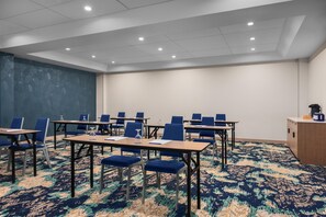 Une salle de conférence avec des tables et des chaises, une moquette à motifs et un mur uni.