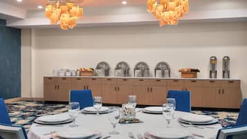 Un salón de conferencias con una larga mesa dispuesta para una reunión, equipado con sillas, platos, vasos y cubiertos.