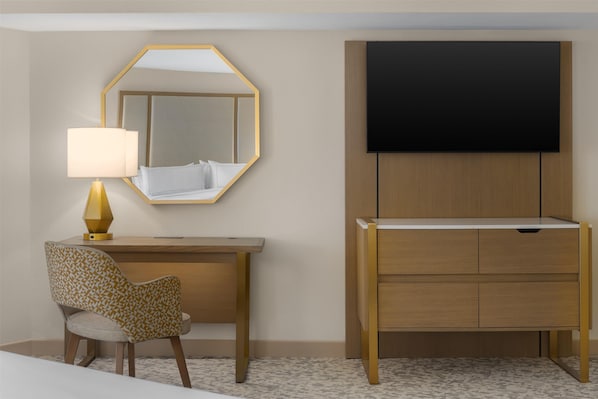 A hotel room with a bed, a desk with a lamp, a chair, a TV, and a wardrobe.