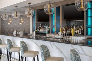 Zona de bar con mostrador de mármol, taburetes y una variedad de botellas de licores.