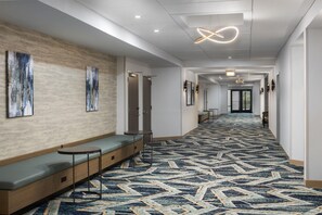 Un vestíbulo de hotel con alfombra estampada, zona de estar, obras de arte y una lámpara moderna.