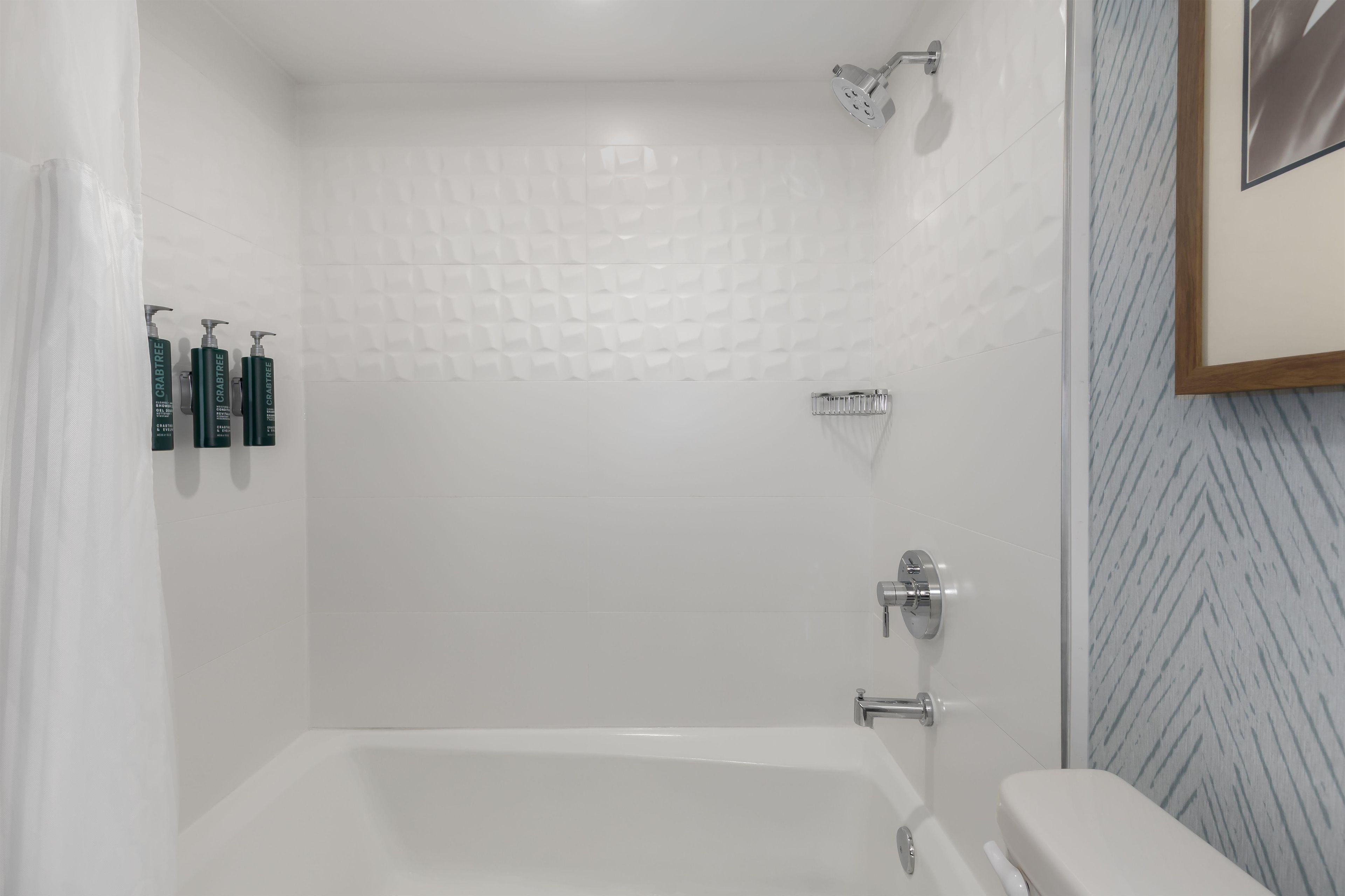 Ein Badezimmer mit einer Badewanne, einer Dusche und einem WC. An der Wand stehen drei Flaschen Crabtree-Produkte.
