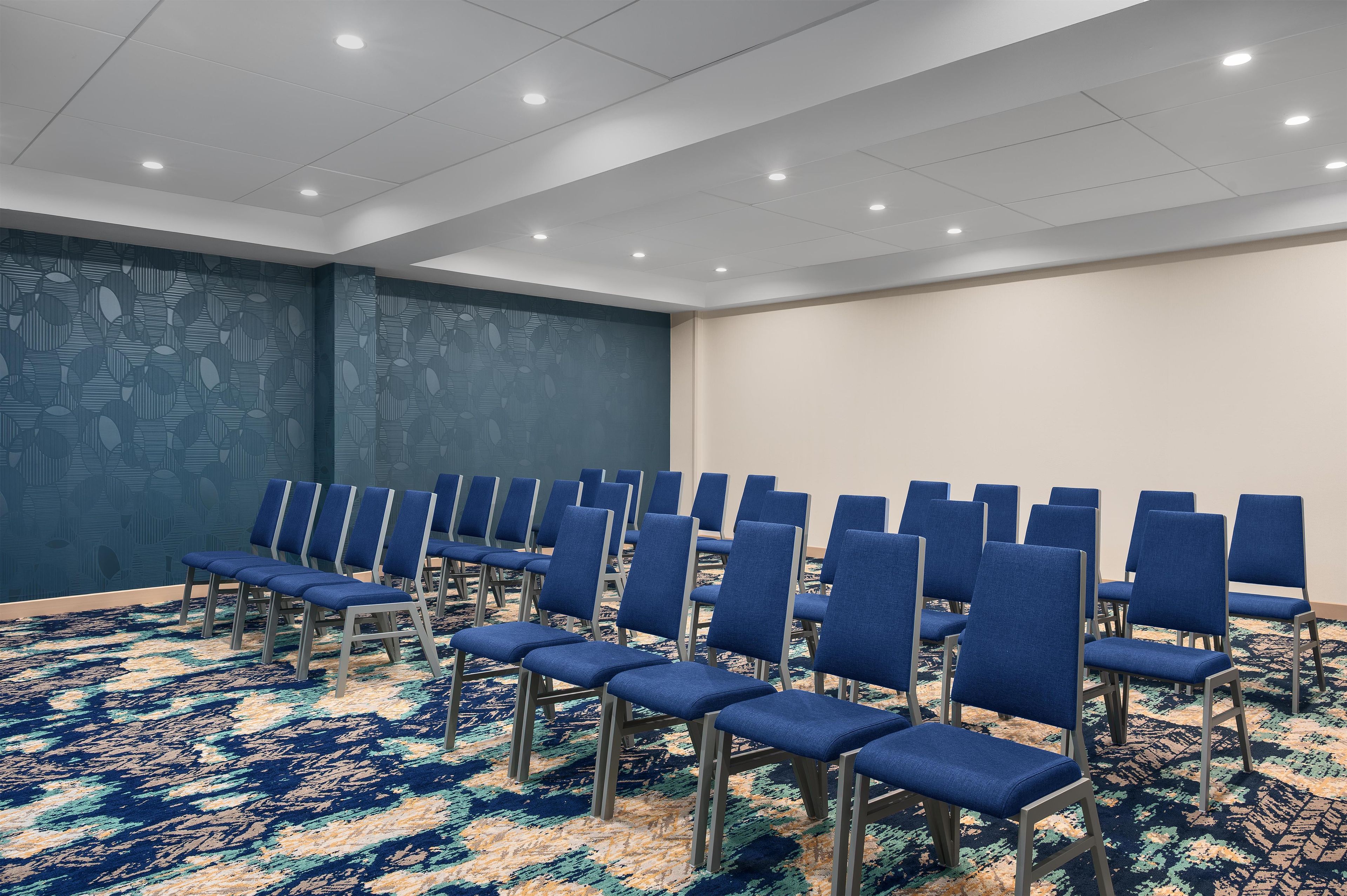 A conference room with rows of blue chairs, a patterned carpet, and a wall with a geometric design.