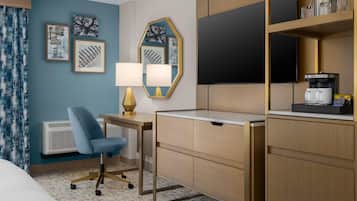 Habitación de hotel con escritorio, silla, televisión de pantalla plana, cafetera y una obra de arte en la pared.