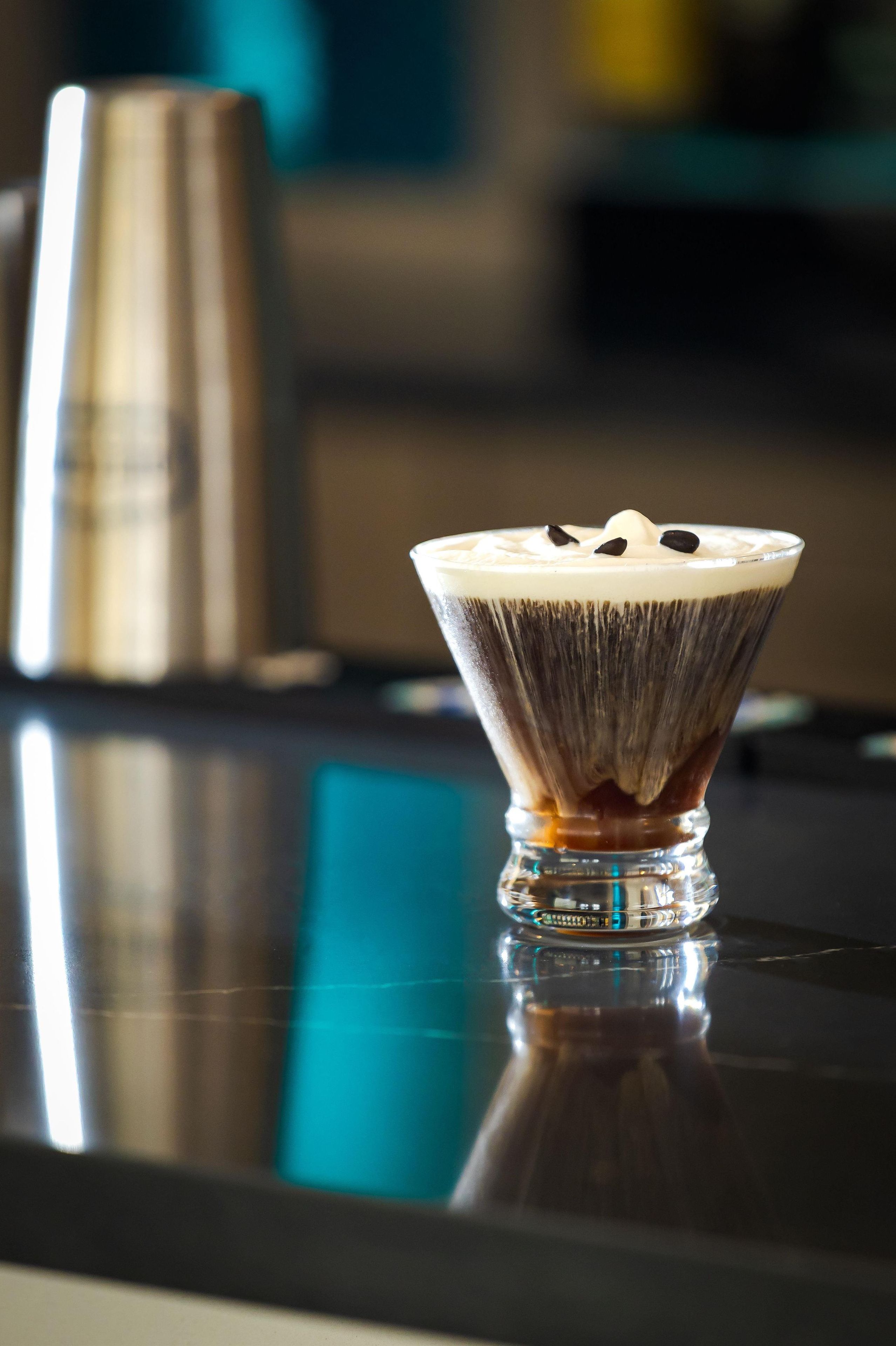 A martini glass with a layered drink on a reflective surface.