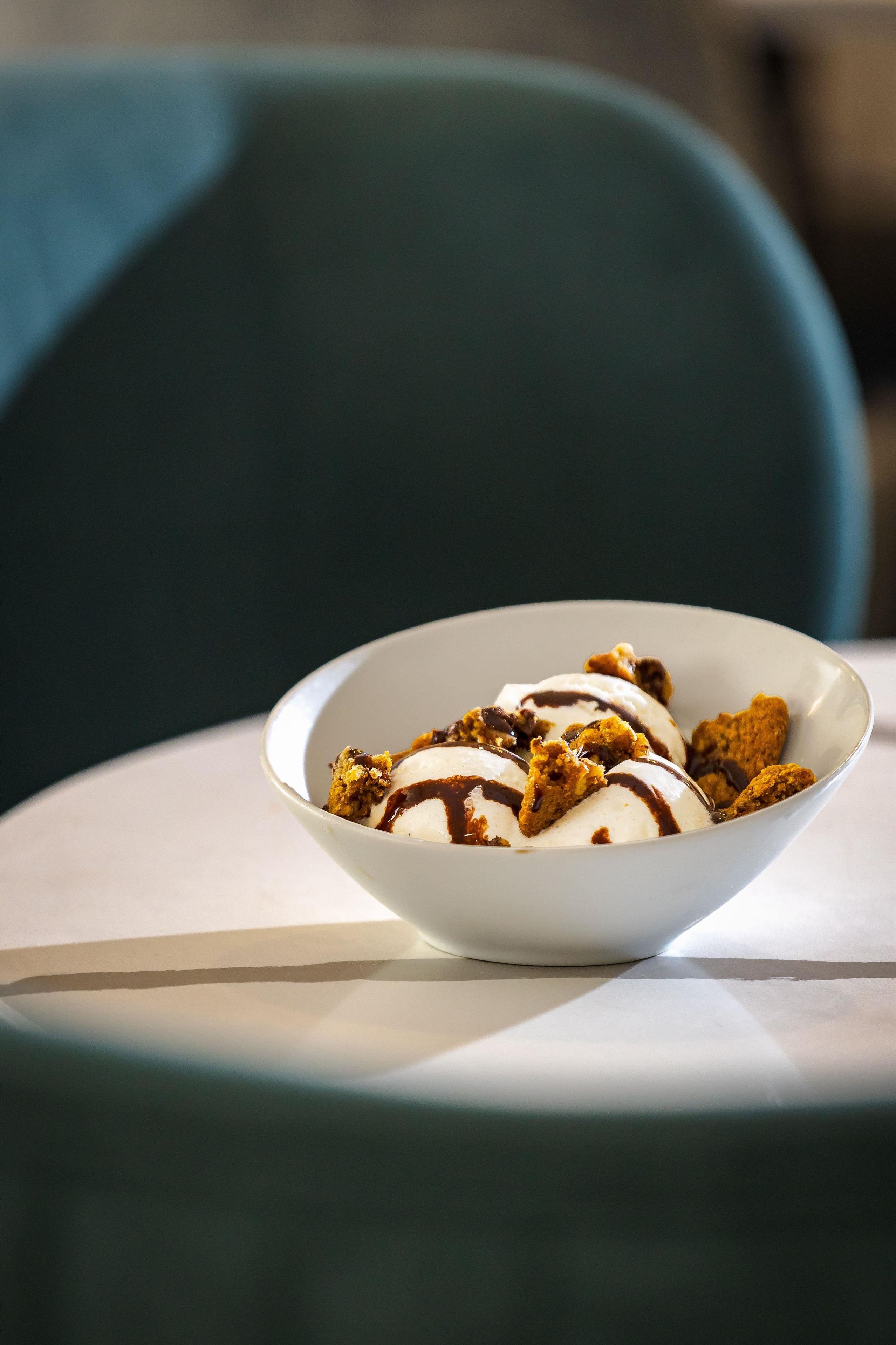 Un bol de dessert avec de la crème glacée et une sauce au chocolat, présenté sur une assiette blanche.