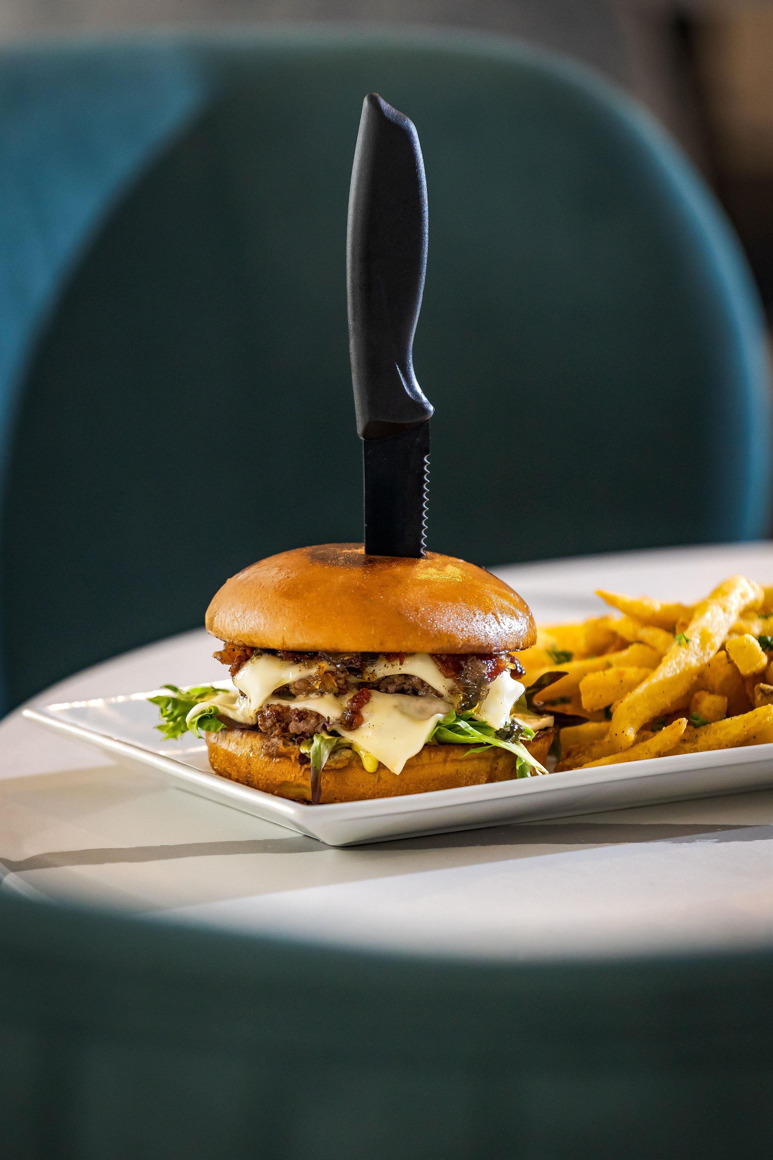 A burger with a knife on top, served with fries on a white plate.