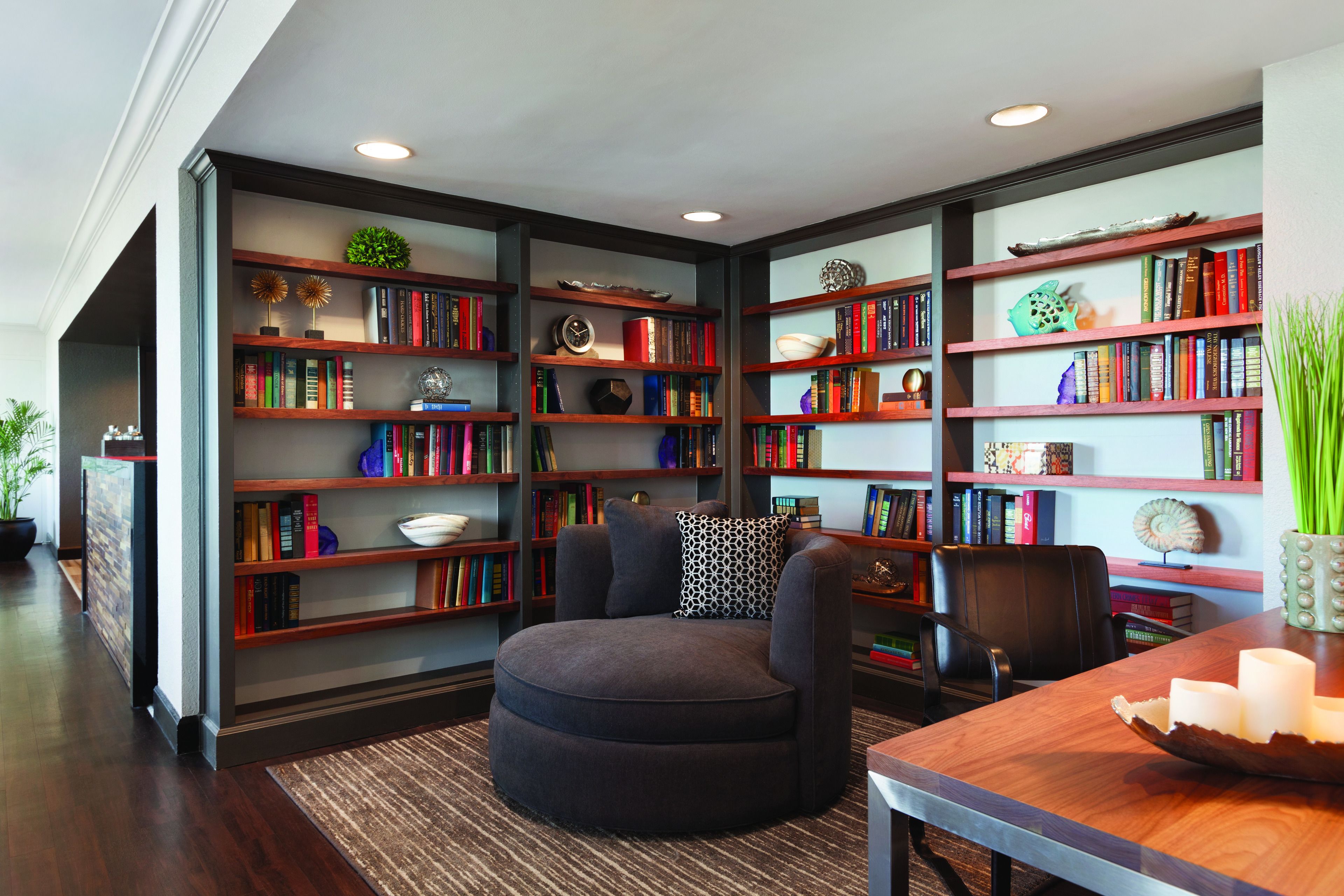 A library with multiple bookshelves, a round ottoman, and a wooden table with a decorative bowl.