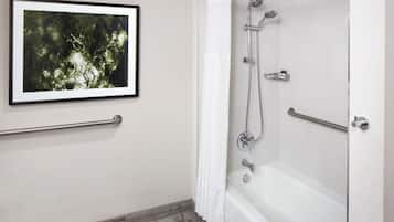A bathroom with a framed picture on the wall, a shower with a curtain, and a grab bar.