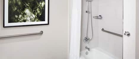 Un baño con un cuadro enmarcado en la pared, una ducha con cortina y una barra de apoyo.