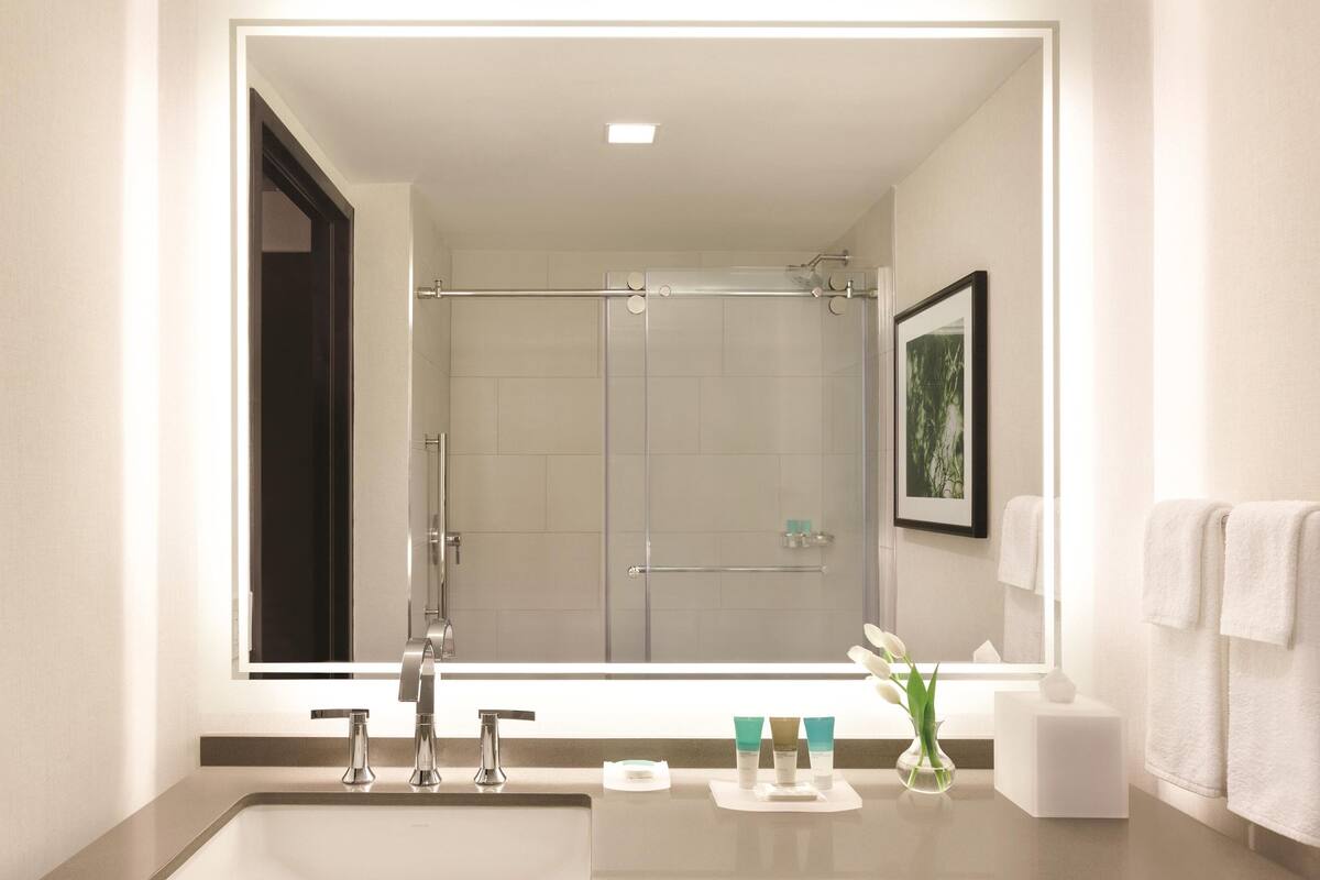 A modern bathroom with a large mirror, a shower, and a sink with toiletries.