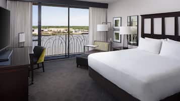 Habitación de hotel con una cama grande, un escritorio, una silla, una mesita y un balcón con vistas a la ciudad.