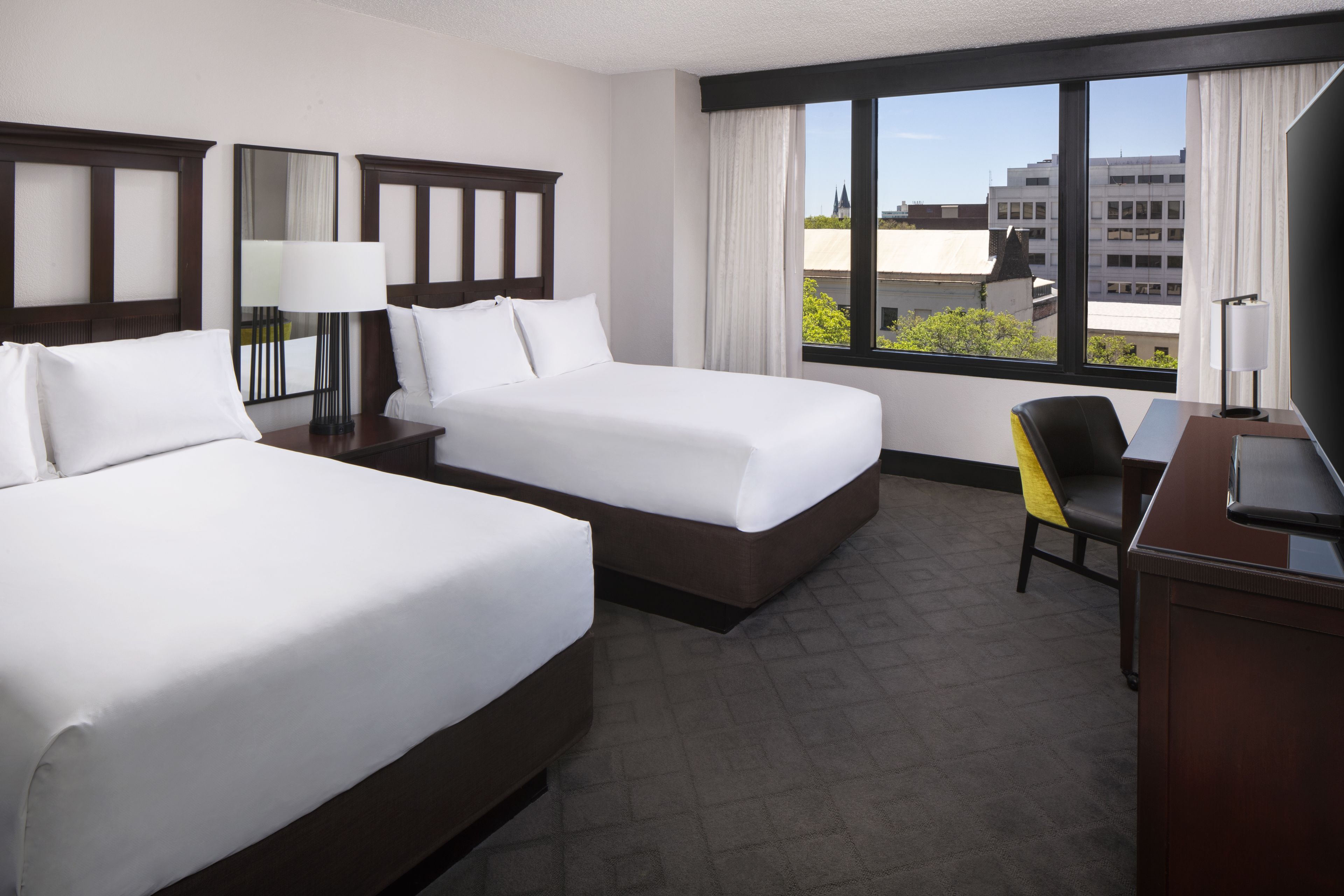 A hotel room with two beds, a desk, and a chair.