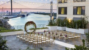A rooftop venue with a view of a bridge and river, arranged with chairs and tables for events. - Hyatt Regency Savannah (Savannah)