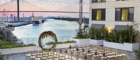 Un espacio en la azotea con vistas a un puente y un río, dispuesto con sillas y mesas para eventos.