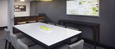 A modern dining area with a marble table, grey upholstered chairs, a yellow patterned pendant light, and a framed abstract painting on the wall.