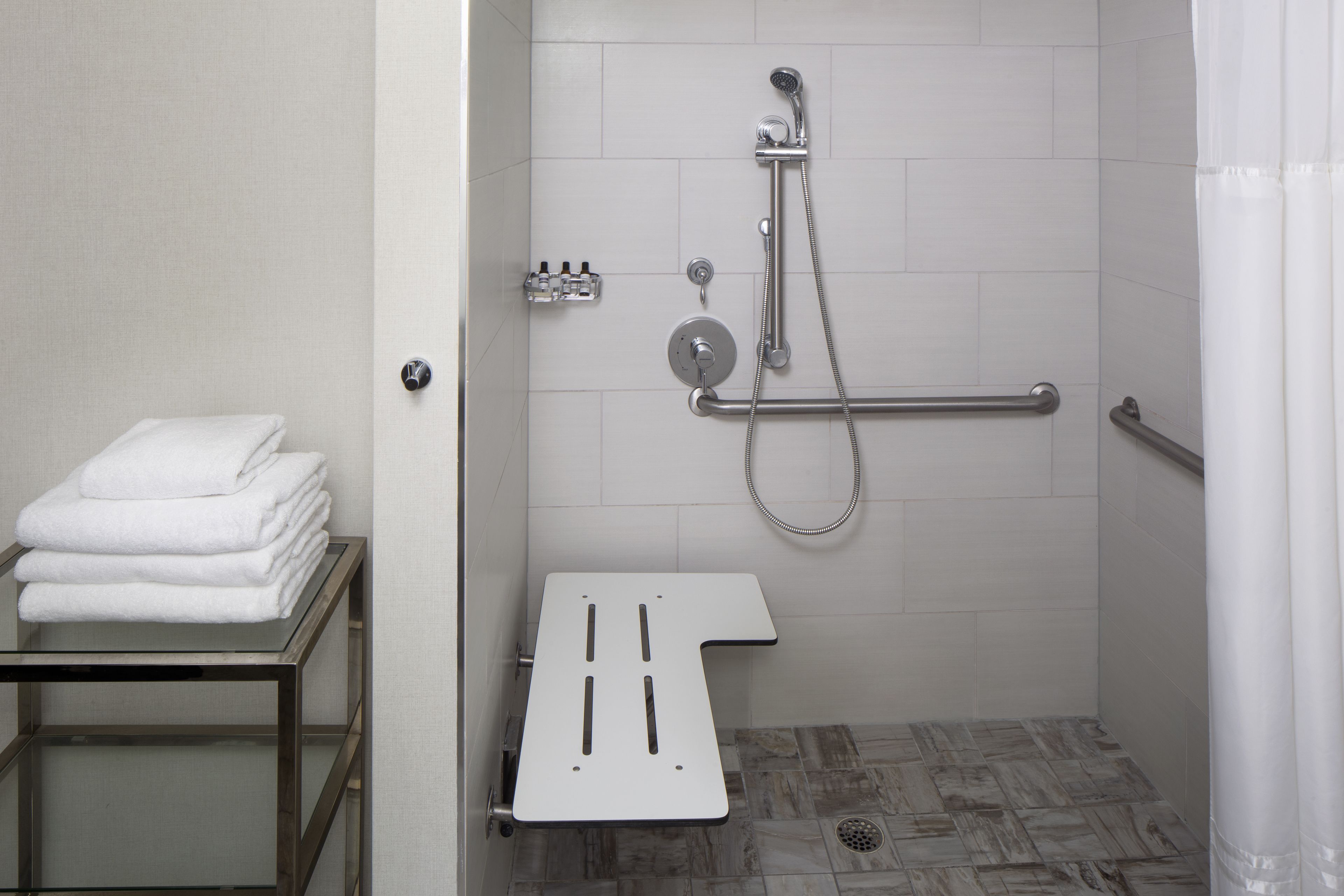 A modern bathroom with a shower, grab bars, and a towel rack.