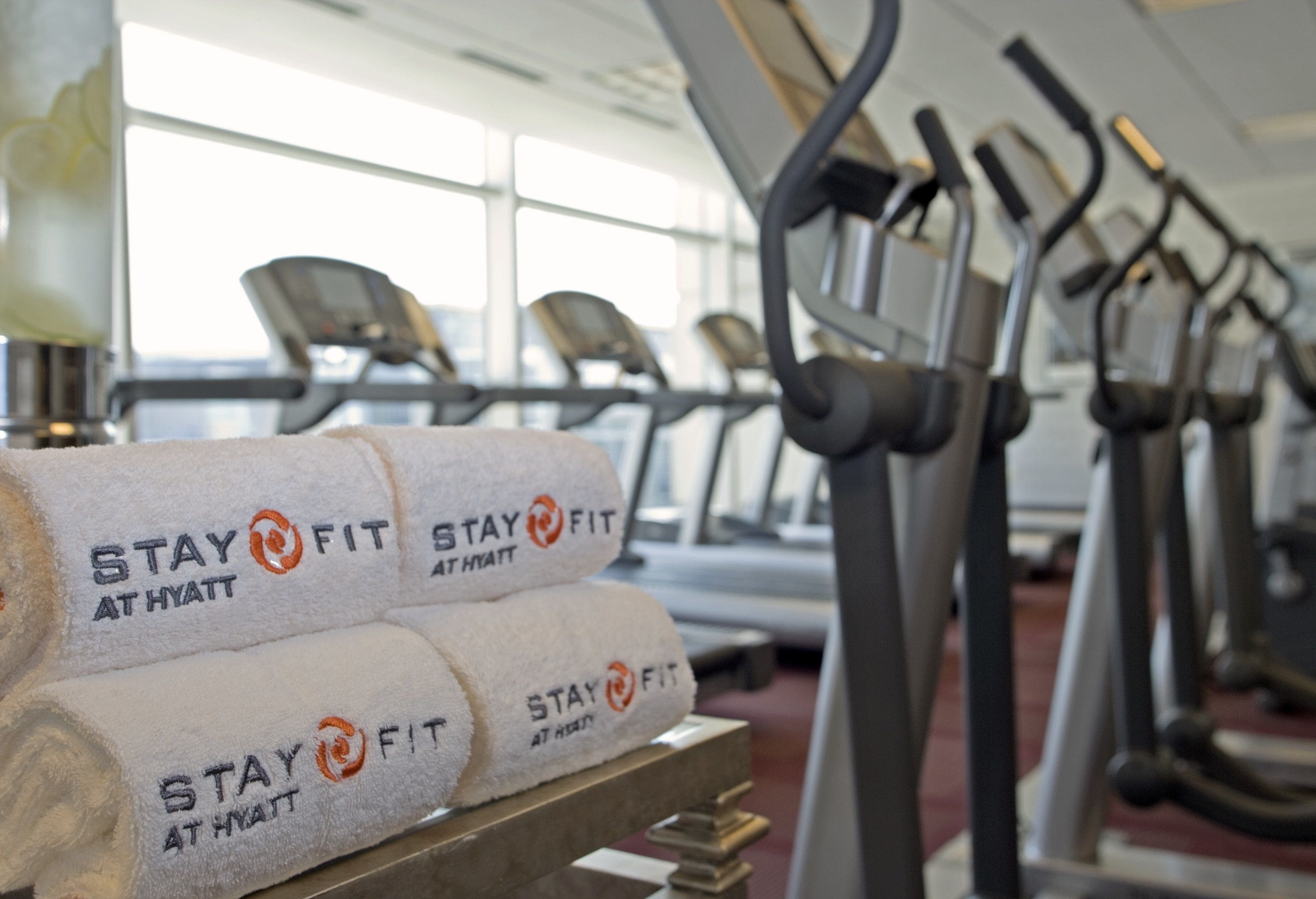 File di tapis roulant in palestra, con asciugamani impilati su un tavolo con la scritta "STAY FIT AT HYATT".
