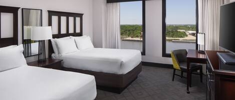 Habitación de hotel con dos camas, un escritorio, una silla, un televisor y ventanas amplias con vistas al exterior.