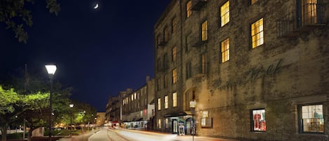Escena nocturna de una calle con vías de tranvía, un edificio con numerosas ventanas y la luna en el cielo.