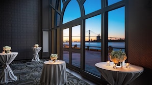 A room with large windows overlooking a bridge and water, featuring tables with floral centerpieces and candles. - Hyatt Regency Savannah (Savannah)