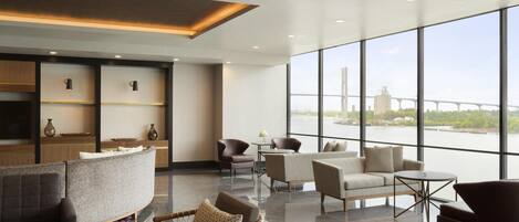A spacious lobby with a seating area, a reception desk, and large windows offering a view of a bridge and water.